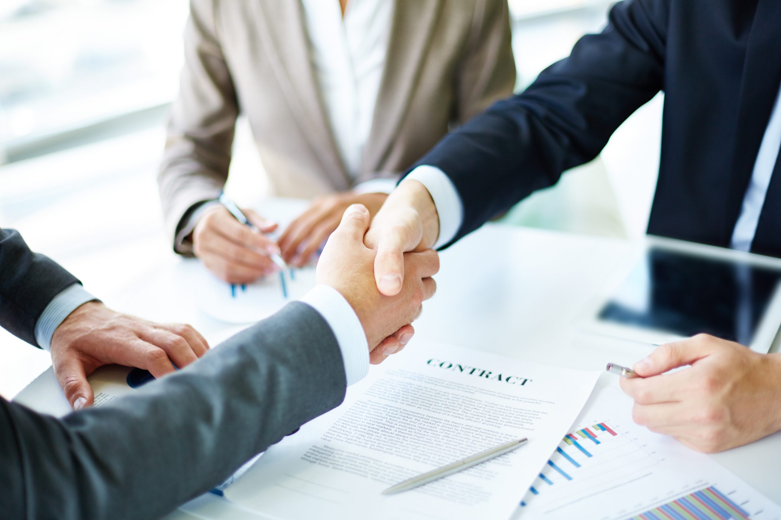 Handshake during executive search negotiation with paper contract in background