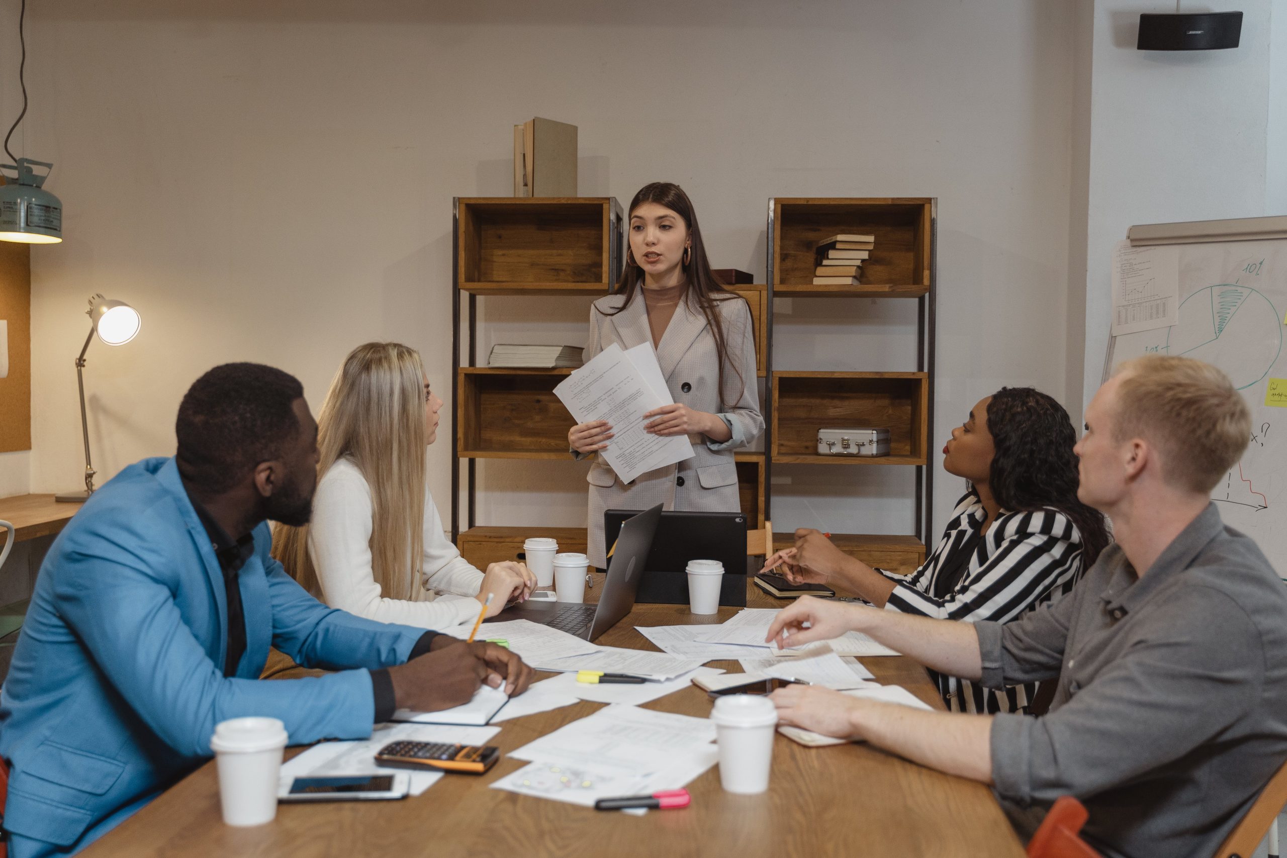 A diverse team in a meeting with a woman leading the discussion on how build teamwork and leadership skills in the workplace