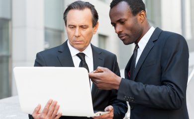 Two professional men in suits discussing what's on the laptop