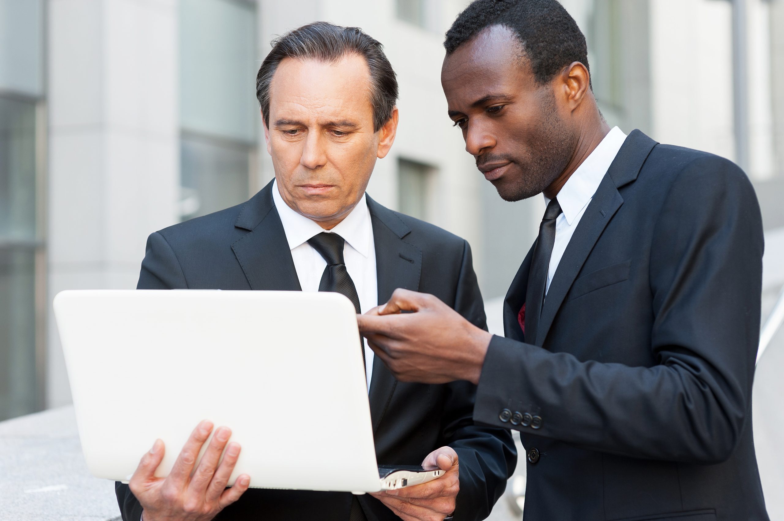 Two professional men in suits discussing what's on the laptop