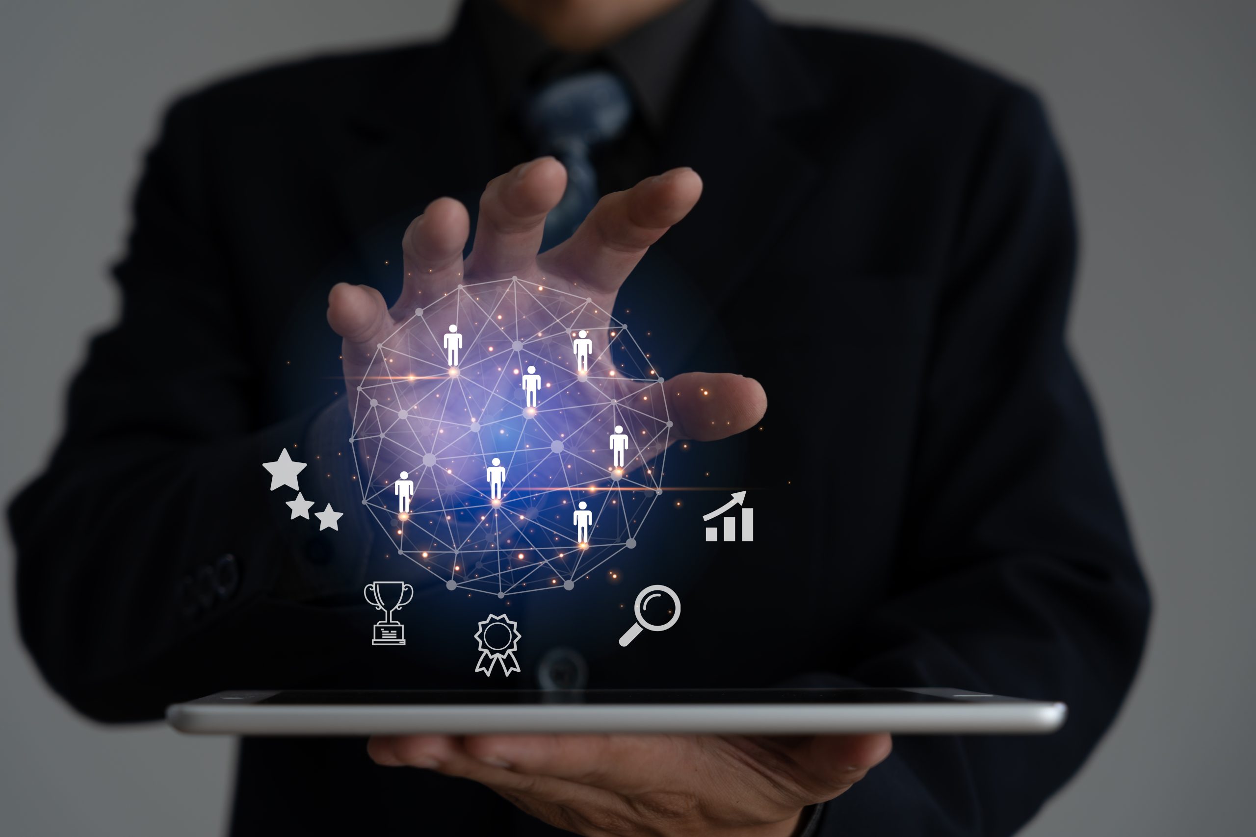 A business professional holding a tablet with a holographic interface above it displaying icons of people.