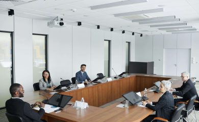 Large white modern meeting with a diverse board sitting and conversing around a large wooden table