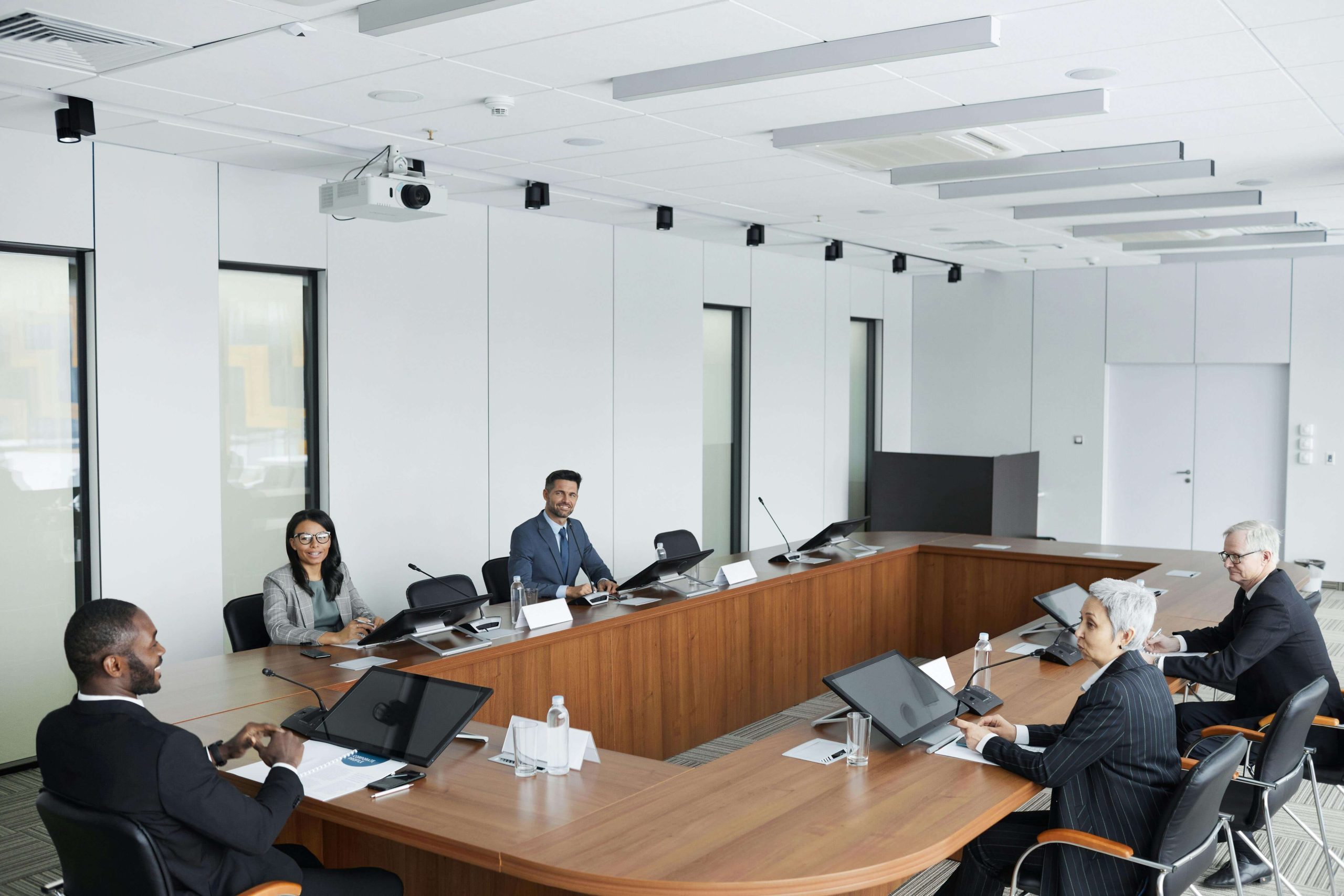 Large white modern meeting with a diverse board sitting and conversing around a large wooden table